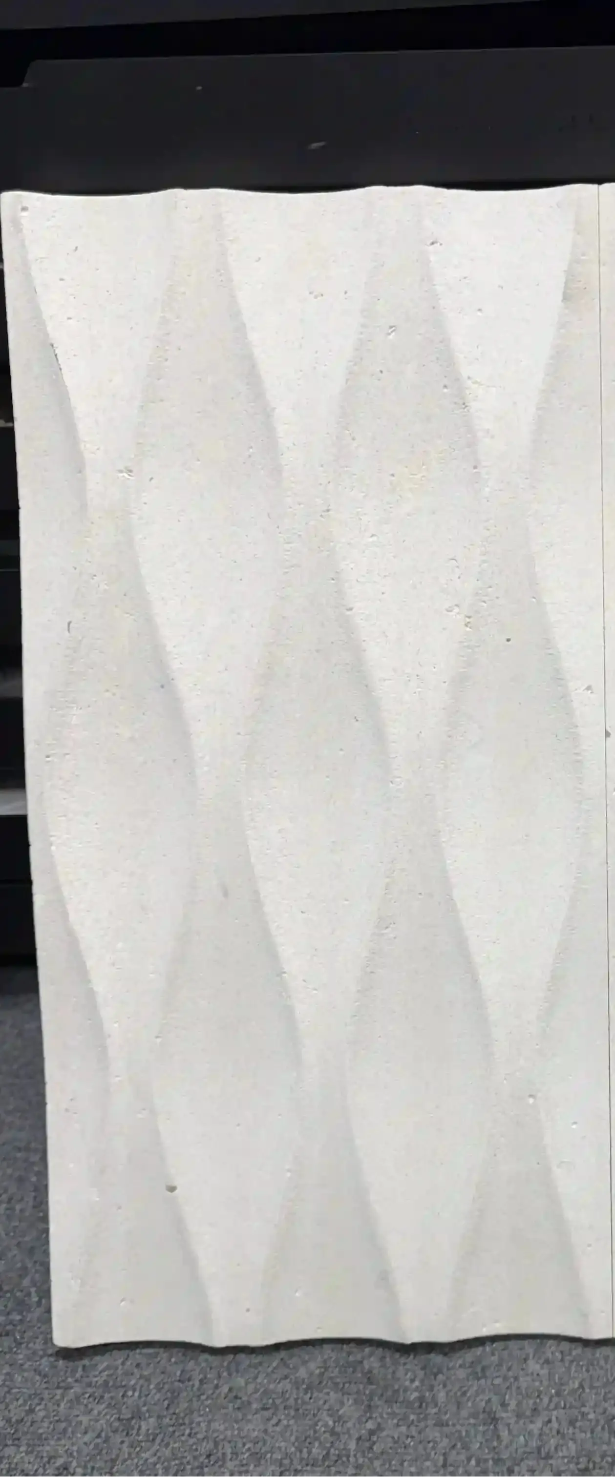 A square off-white textured tile with a 3D geometric diamond pattern, displayed against a dark background.