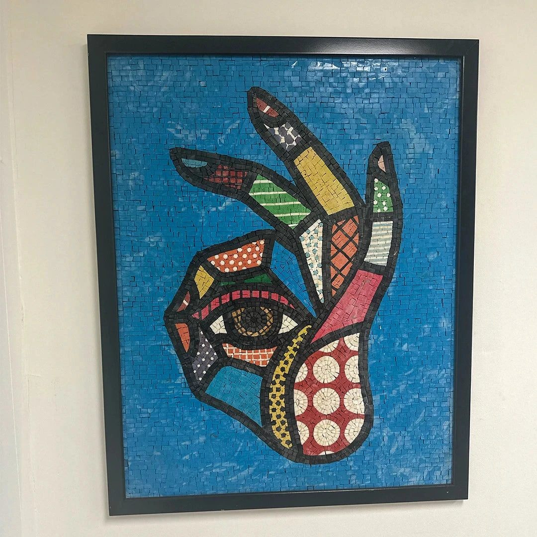 Colorful mosaic artwork of a hand with fingers extended on a blue background, framed in black.