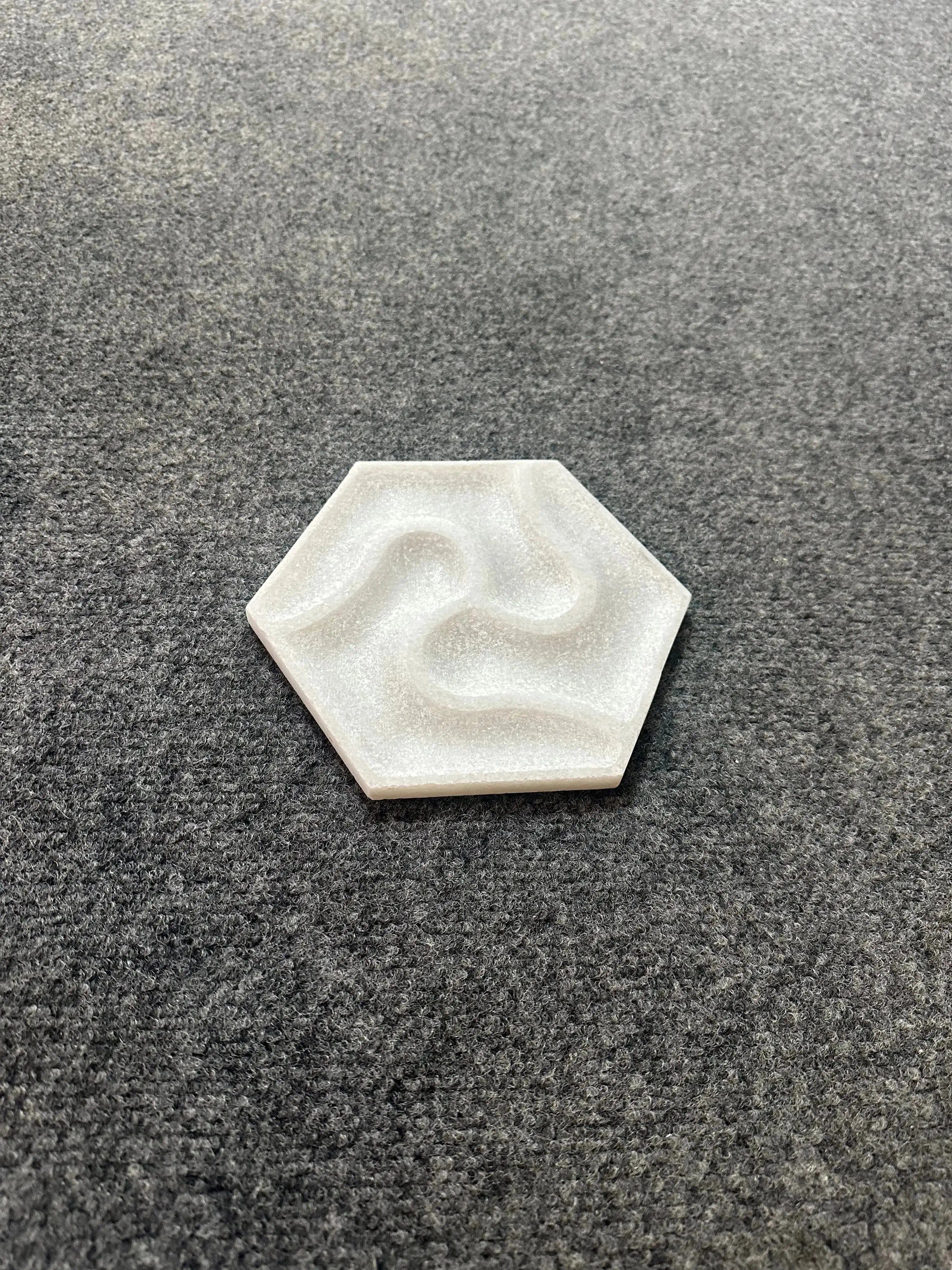Hexagonal white stone with a wavy pattern on a gray textured surface