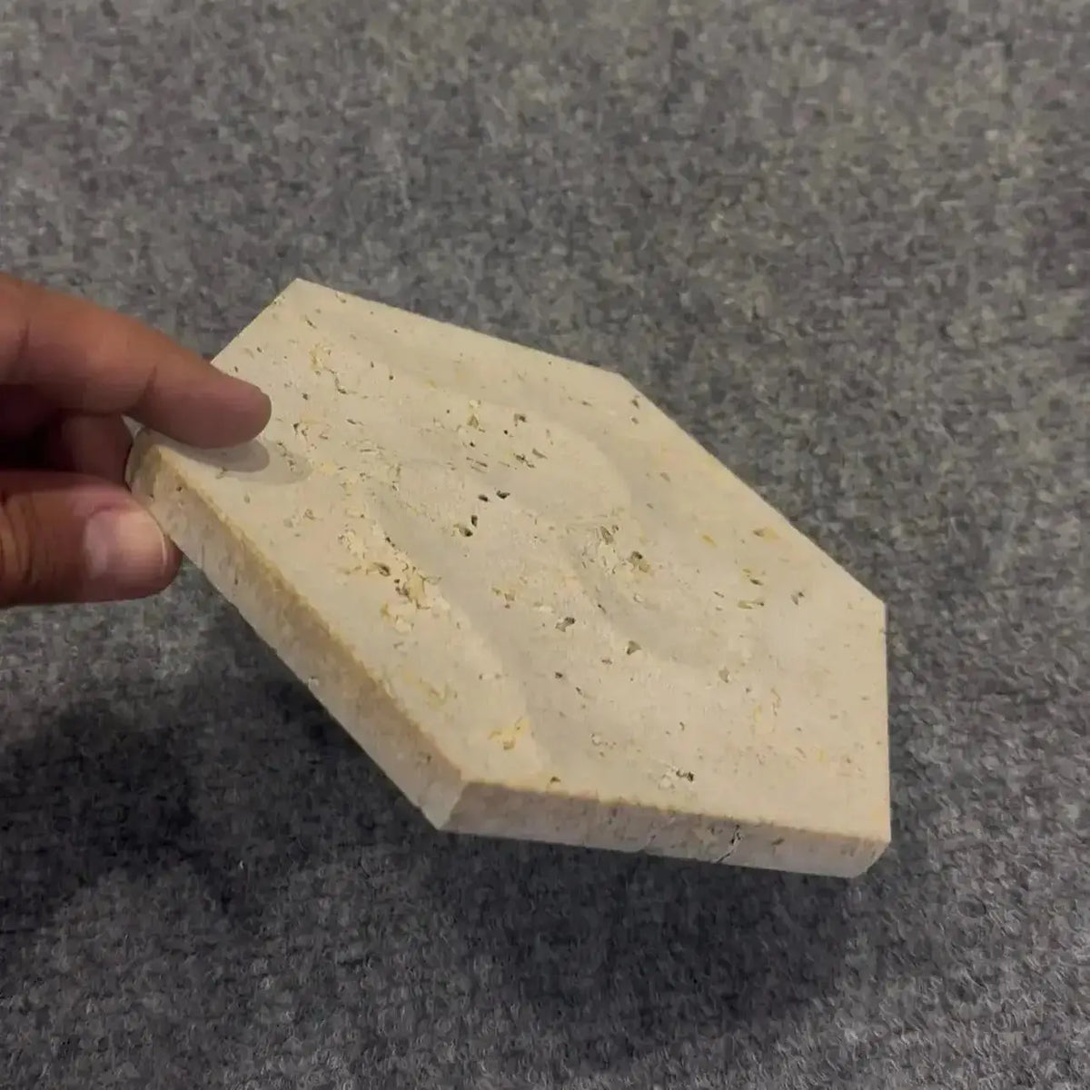 Hexagonal stone block held by a hand on a gray background bathroom tile - wall tile - kitchen tile - backsplash