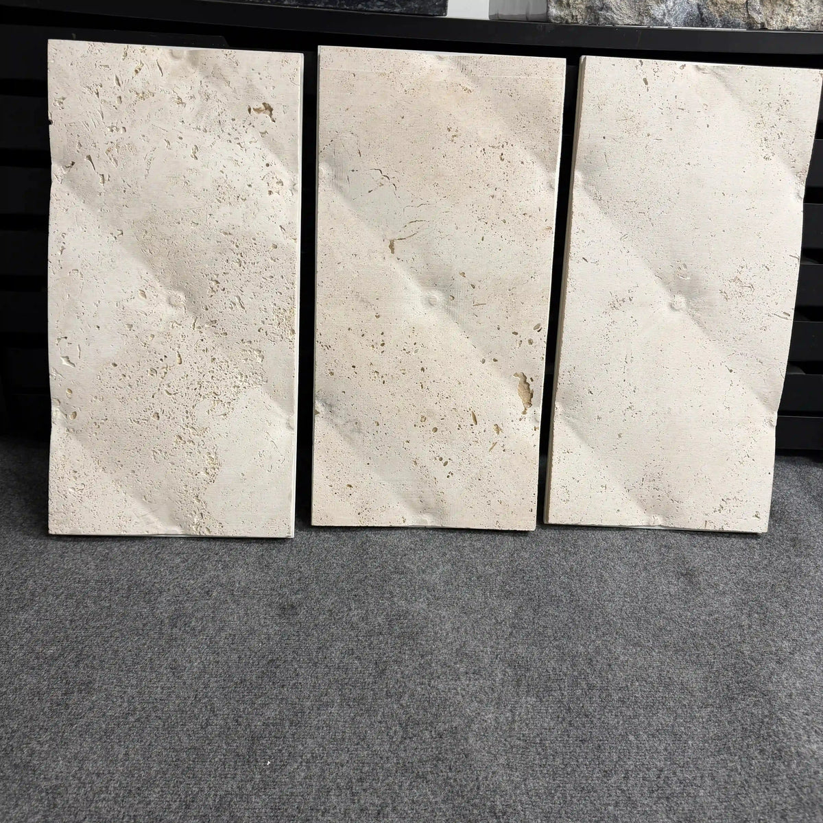 Griffin natural stone 3D wall panels displayed as a set of three vertical tiles, showcasing a minimalist geometric faceted surface with diagonal folded planes in a warm beige or travertine-like finish featuring natural organic pores.
