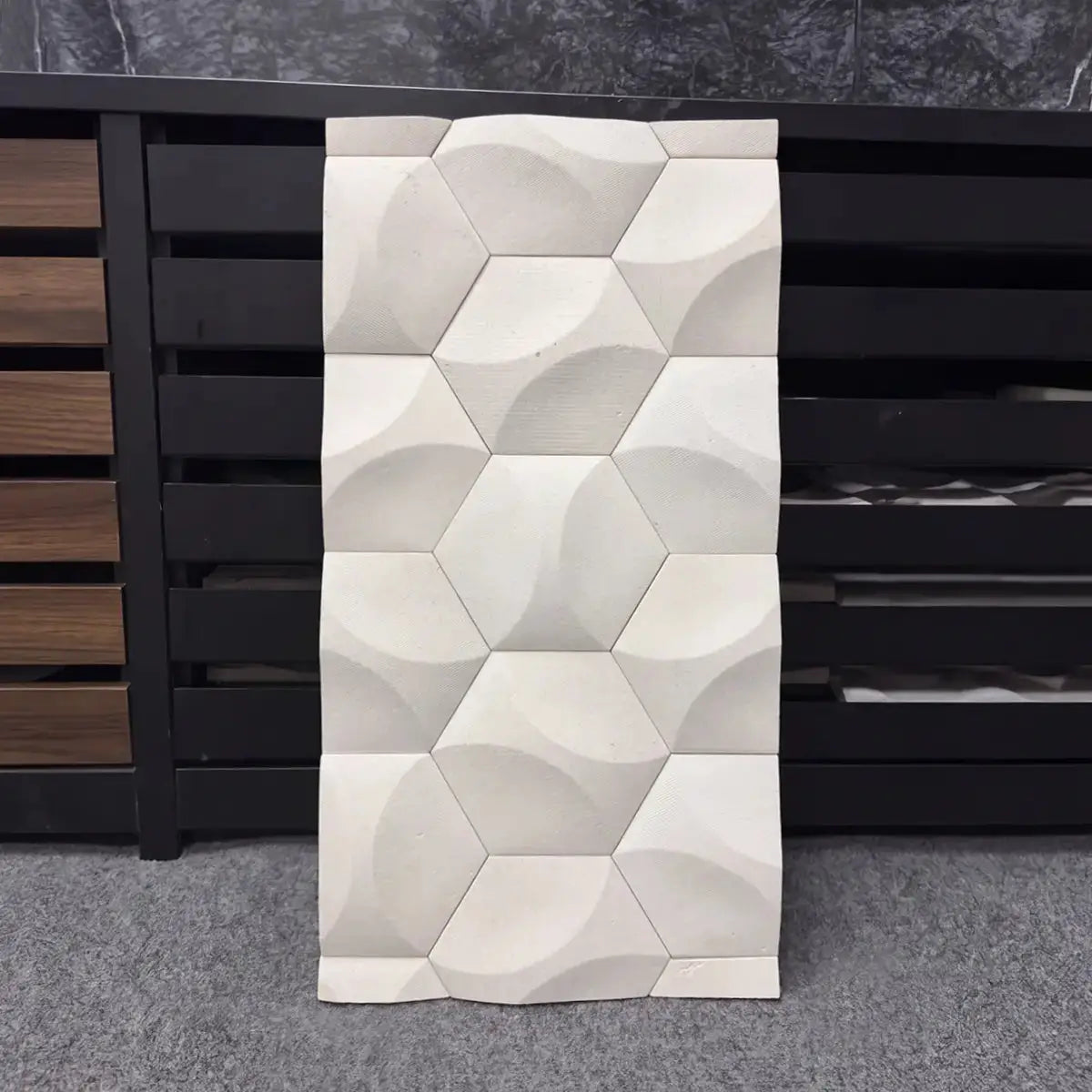 Orbis natural stone mosaic tile sample displayed vertically against a dark background, highlighting its repeating geometric hexagonal pattern with concave carved facets and a clean matte white limestone surface.