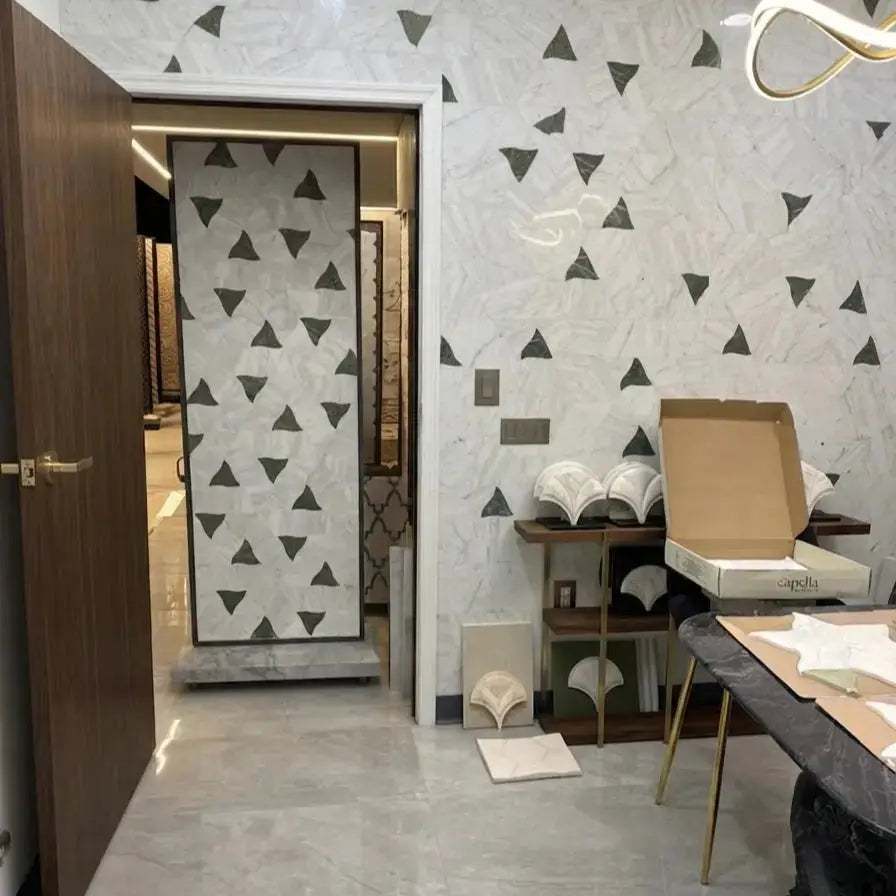 Selena natural stone mosaic tile showcased in an interior showroom setting with a feature wall and matching display panel installed with abstract geometric triangular patterns in white marble and dark grey or green stone accents.