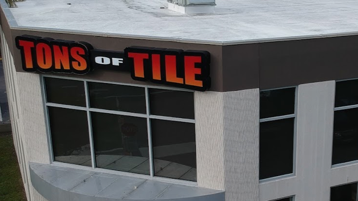 Storefront with 'TONS OF TILE' sign and sale signs on windows