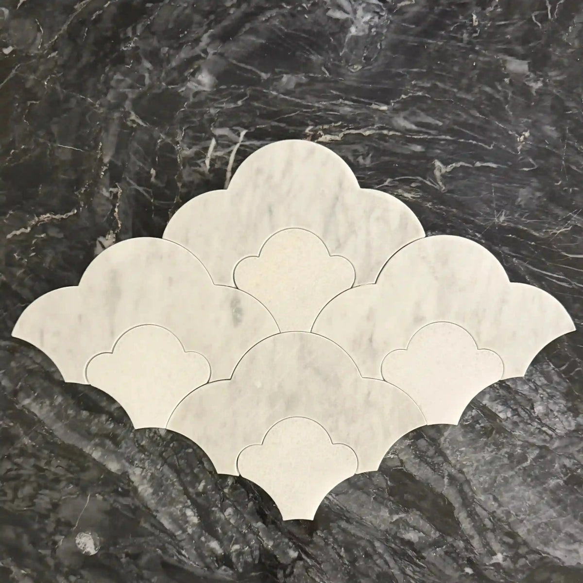 Tiara natural stone mosaic tile arranged as a scalloped, overlapping pattern featuring curved interlocking shapes in a combination of white marble and lighter beige stone elements set against a dark marbled background.