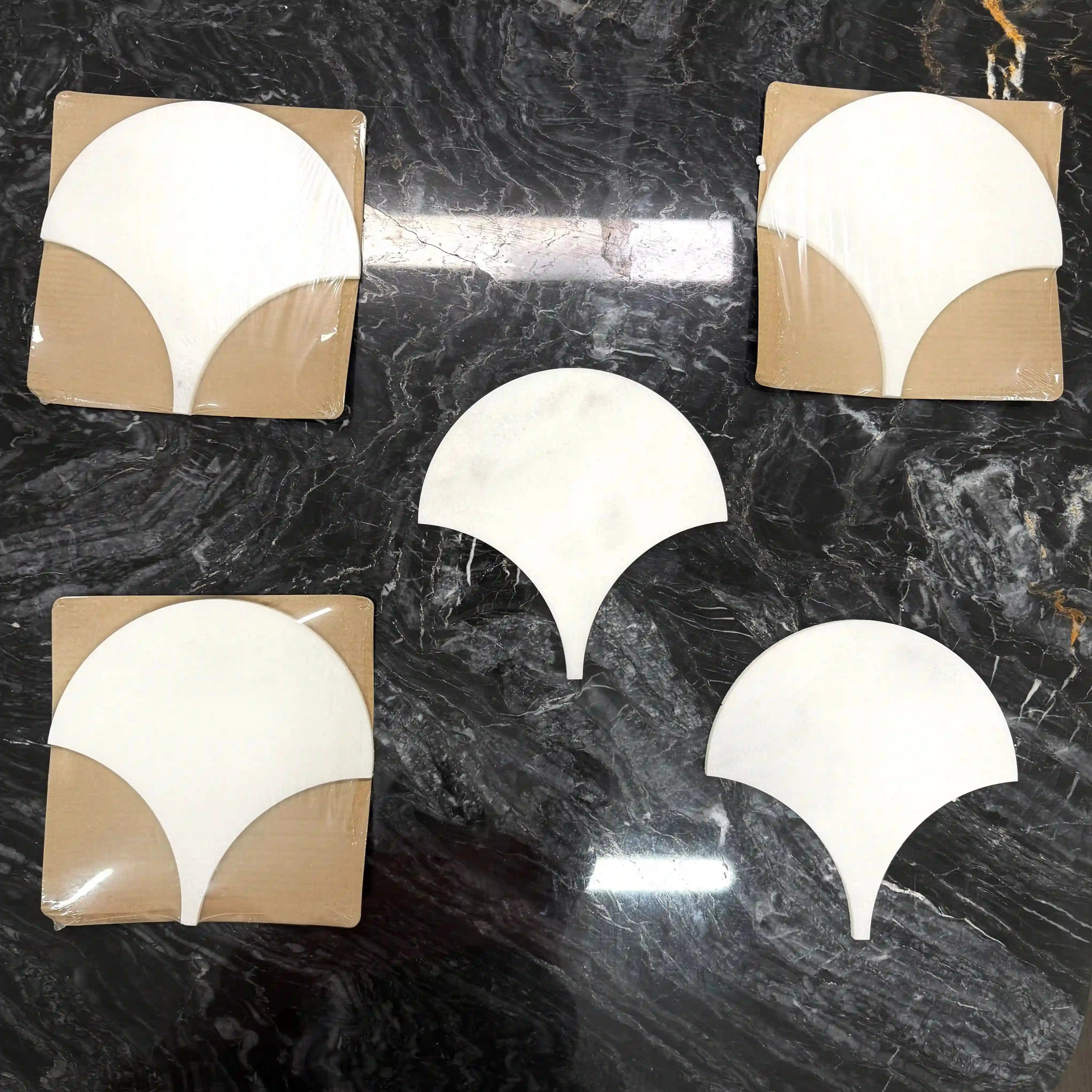 Ebisu natural marble mosaic tiles arranged in a multi-piece display on a dark marble surface, featuring elegant, fan-shaped or teardrop silhouettes with a tapering point in smooth, uniform white marble.