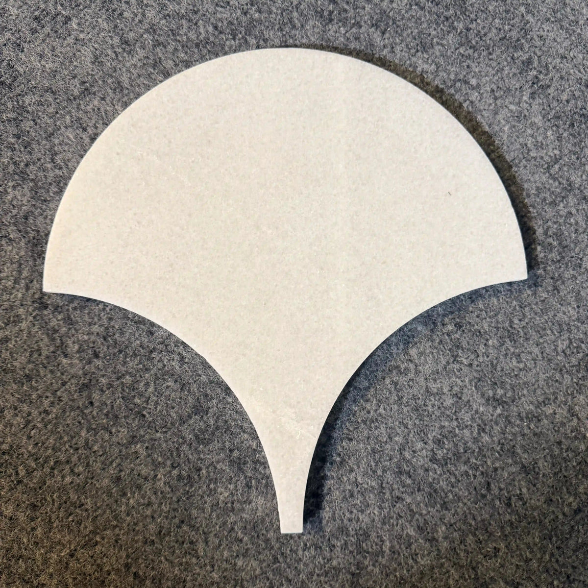 Ebisu natural marble mosaic tile presented as an individual sample piece on a textured gray background, featuring an elegant, fan-shaped or teardrop silhouette with a tapering point in smooth, uniform white marble.