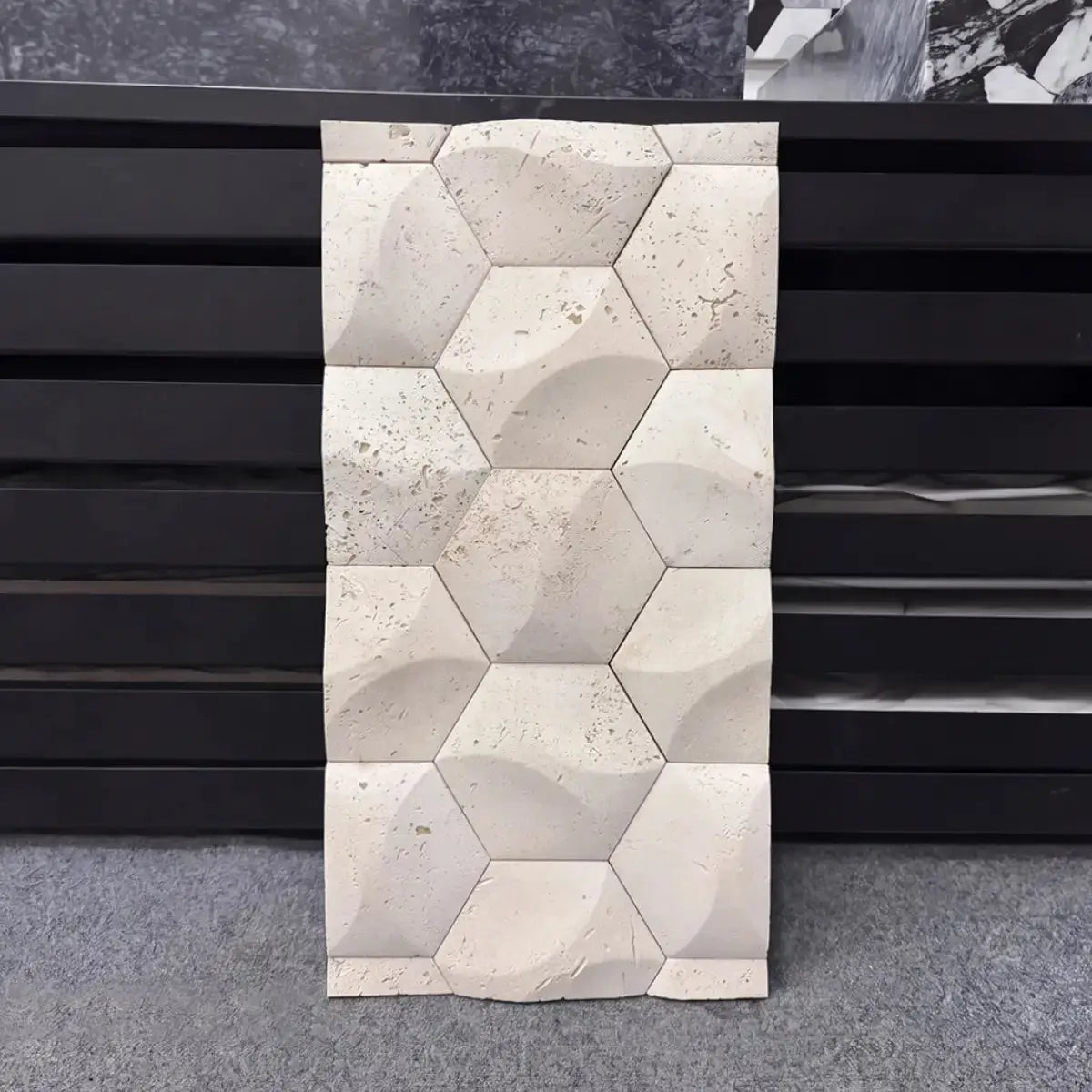 Orbis natural stone mosaic tile sample displayed vertically against a dark background, showcasing its repeating geometric hexagonal pattern with concave carved facets and a natural textured beige travertine surface.