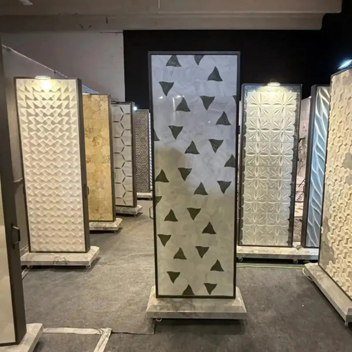 Selena natural stone marble mosaic tile sample displayed on a vertical panel in a showroom, highlighting its scattered triangular pattern across a light marble background.