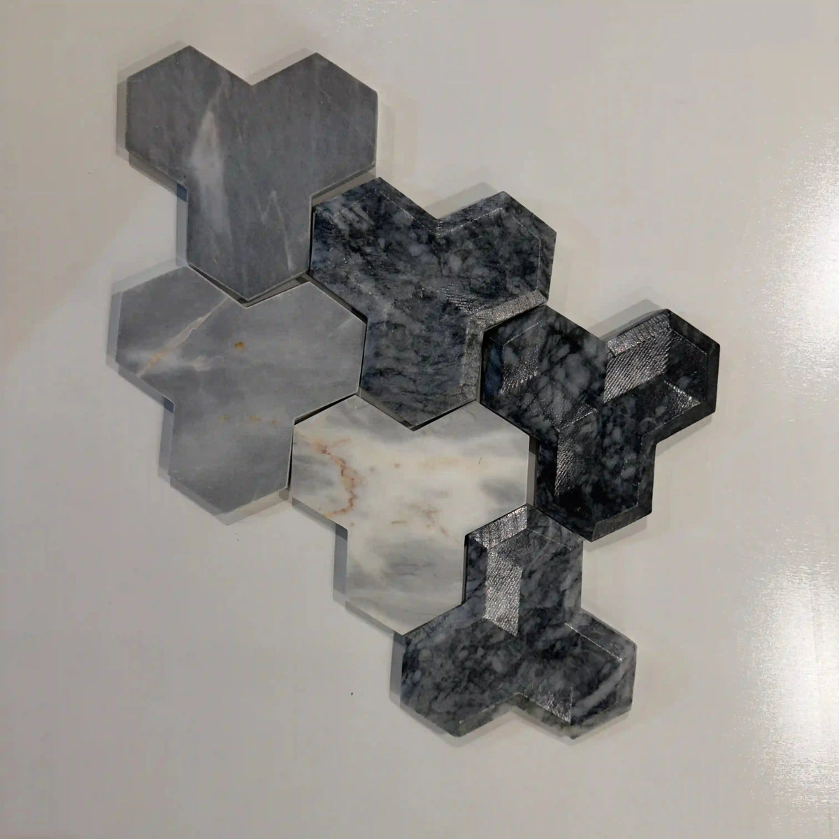 Tabu natural stone 3D wall tile displayed as a multi-toned arrangement of interlocking Y-shaped marble pieces featuring striking variations in white, grey, and dark blue-grey tones with intricate veining.